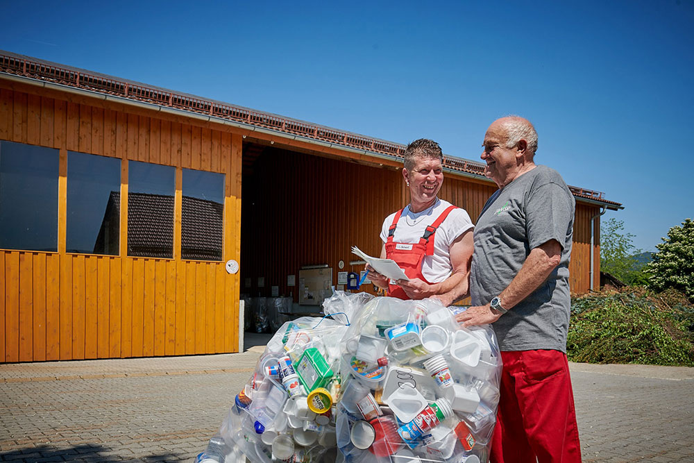 Zwei Mitarbeiter eines Wertstoffhofs mit vollen Kunststoffsäcken